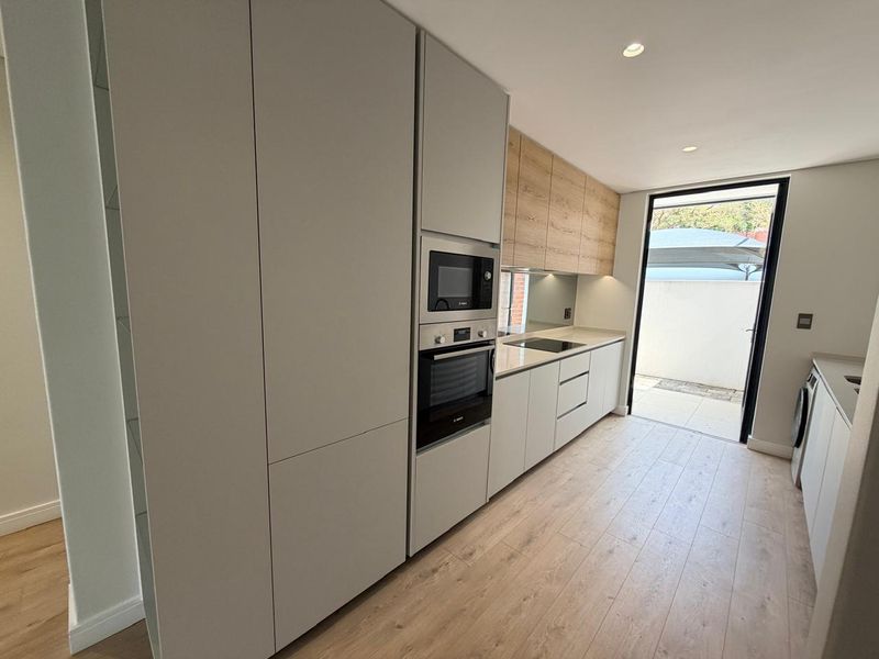 Modern kitchen featuring sleek handleless cabinetry, built-in appliances, and light wood-look flooring with direct access to an outdoor patio area.