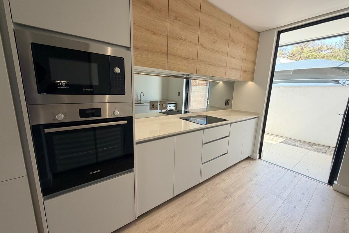 Modern kitchen featuring light wood-tone cabinetry, stone countertops, integrated Bosch appliances, and a mirror splashback, with direct access to an outdoor patio area.