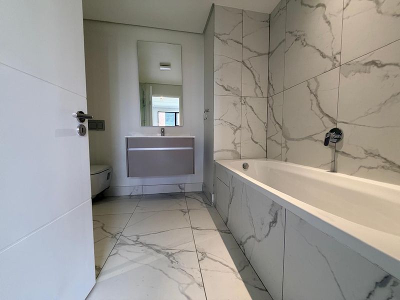 Modern bathroom featuring marble-look floor and wall tiles, a wall-mounted vanity, and a built-in bathtub with chrome fixtures.