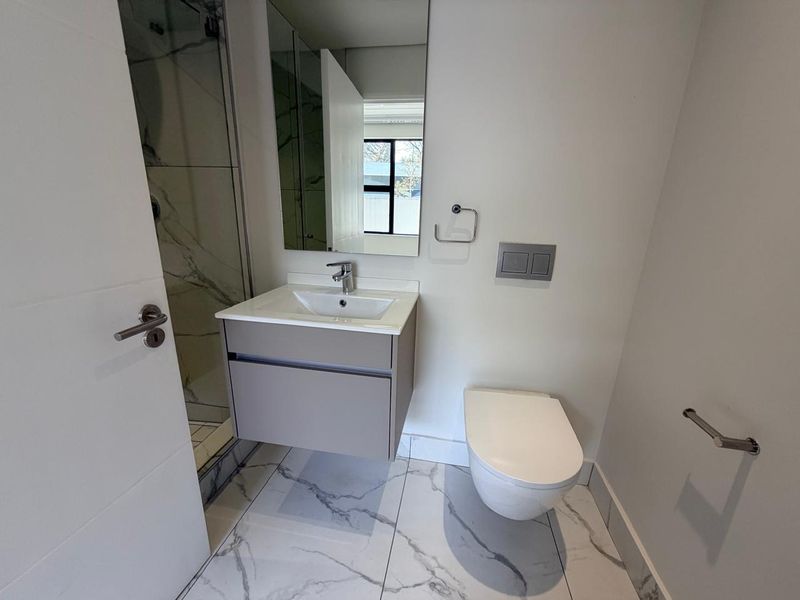 Modern bathroom featuring a wall-hung vanity, wall-hung toilet with concealed cistern, and a walk-in shower with marble-look floor tiles.