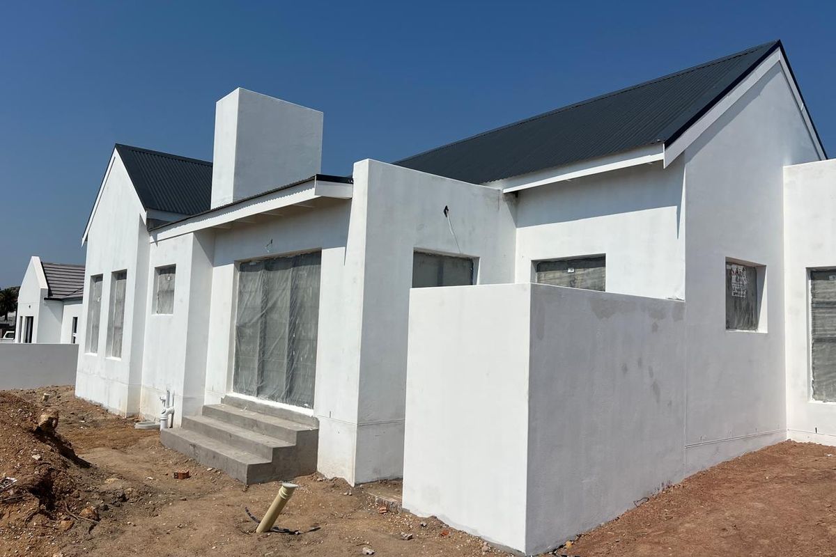 Rear view of a newly constructed house featuring a metal roof, chimney, and unfinished exterior landscaping.