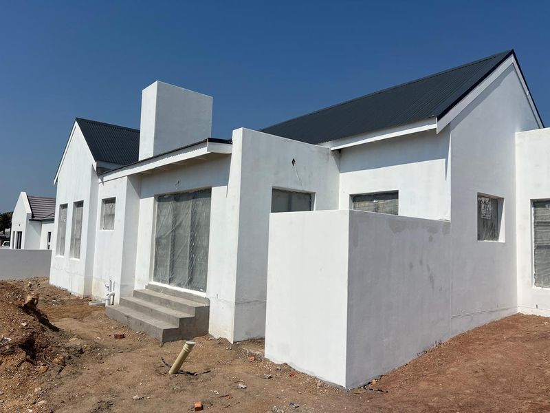 Rear view of a newly constructed house featuring a metal roof, chimney, and unfinished exterior landscaping.