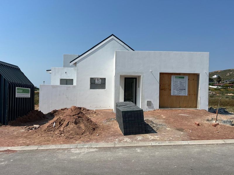 Front elevation of a modern house under construction, featuring a white rendered facade, pitched roof section, and unfinished driveway area.