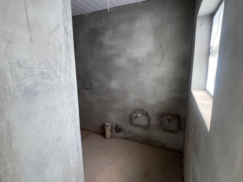 An unfinished laundry room space featuring exposed concrete walls, plumbing rough-ins, and installed ceiling panels, ready for final finishes and fixtures.