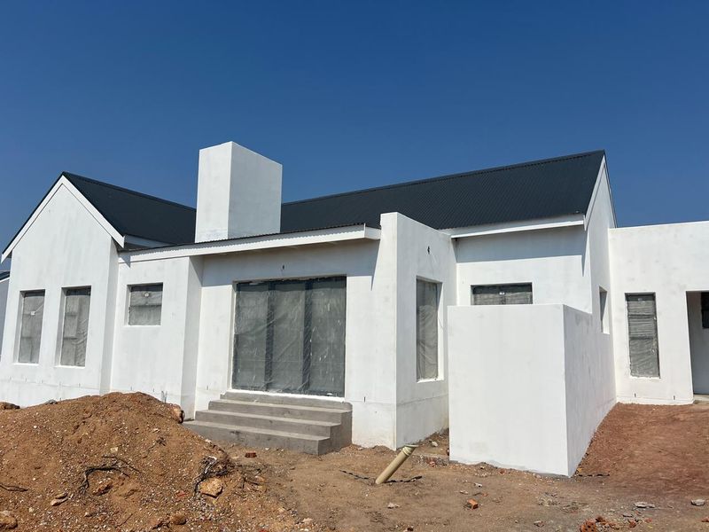 Rear view of a newly constructed modern home featuring a dark corrugated metal roof, white plastered walls, and concrete entrance steps.