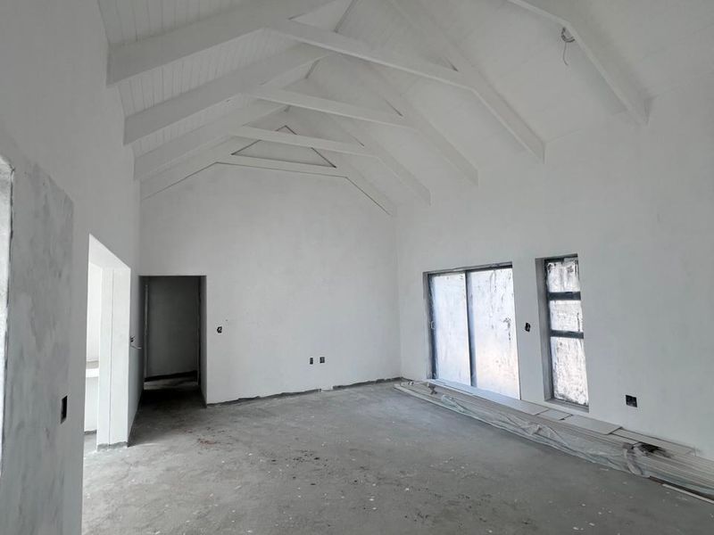 An expansive, unfinished living area featuring a high vaulted ceiling with exposed timber trusses, concrete flooring, and large sliding glass doors.