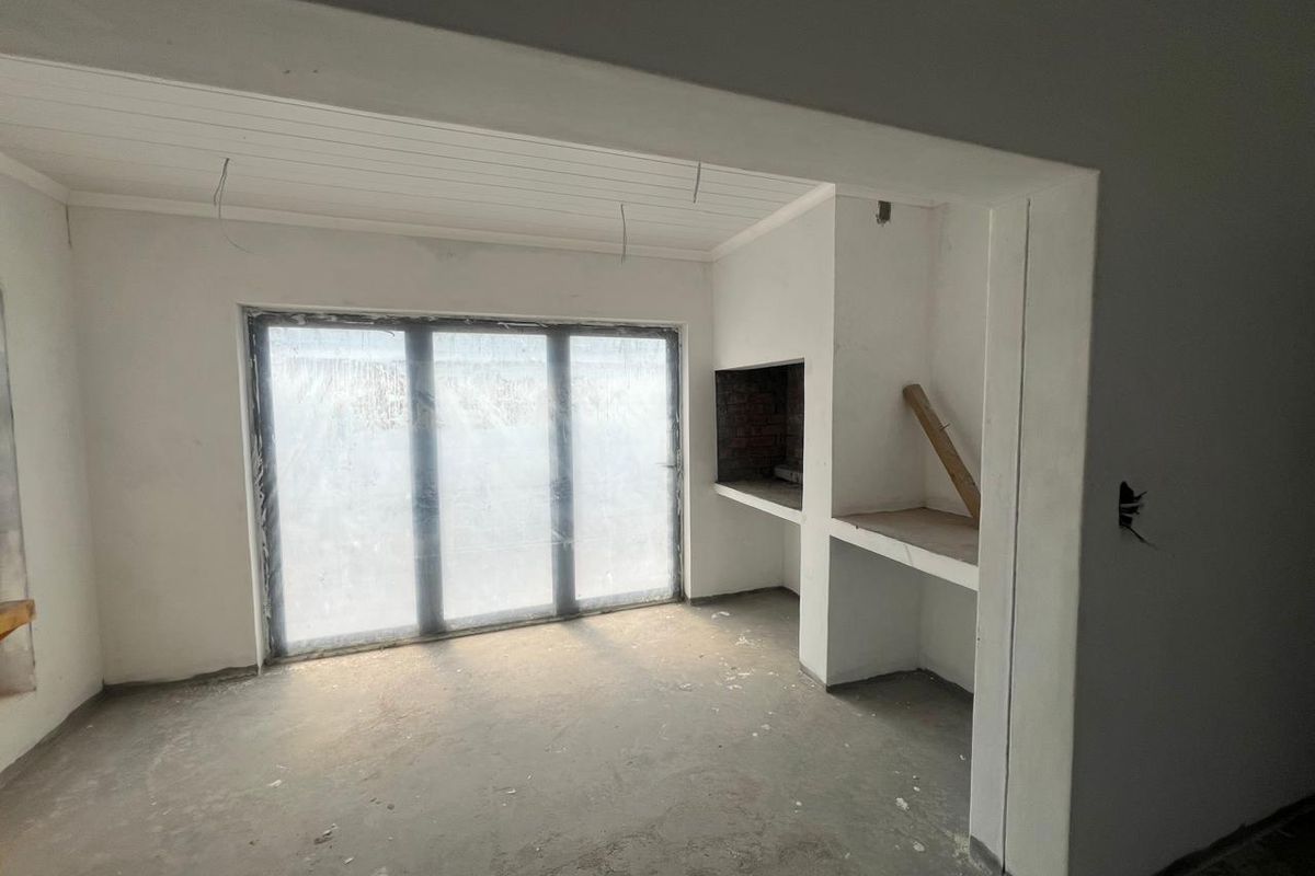 An unfinished living area featuring a built-in fireplace, concrete flooring, and large sliding glass doors leading to the exterior.