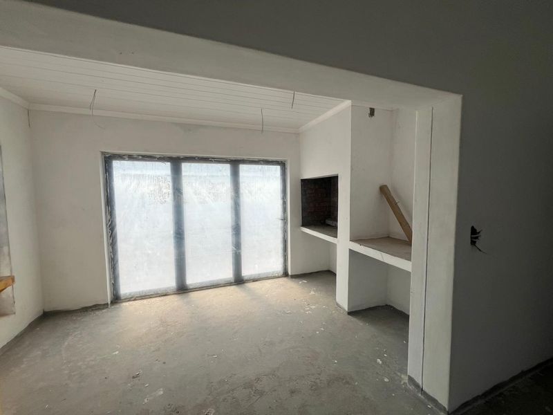 An unfinished living area featuring a built-in fireplace, concrete flooring, and large sliding glass doors leading to the exterior.