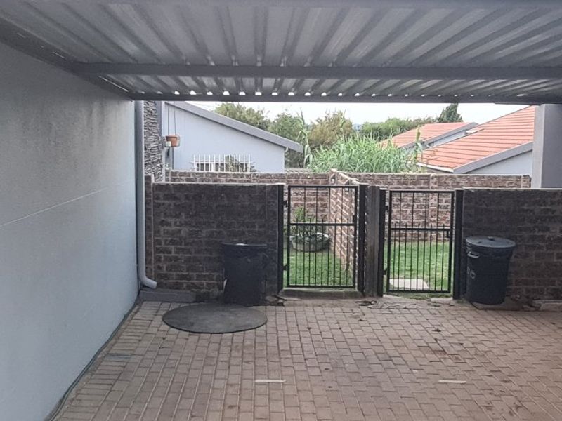 A covered parking area featuring paved flooring, a corrugated metal roof, and a gated entrance leading to a small rear garden space.