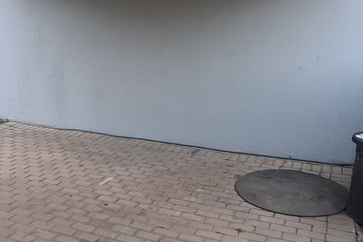 A paved rear patio area featuring a plain exterior wall, downpipe, and external water connection point.