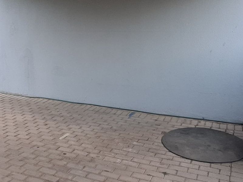 A paved rear patio area featuring a plain exterior wall, downpipe, and external water connection point.