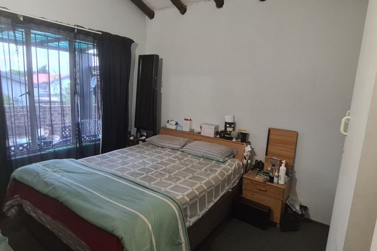 A bedroom featuring exposed timber ceiling beams and a window fitted with security bars, providing a functional living space.