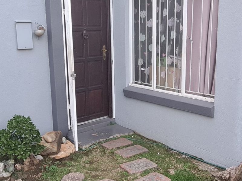 Front entrance of the apartment featuring a timber door, security gate, and window security bars on a painted exterior wall.