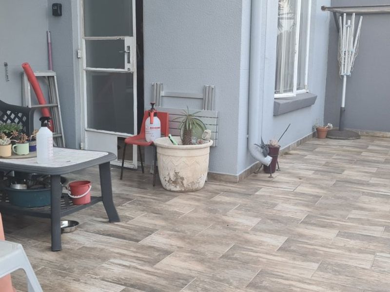 A paved outdoor patio area featuring wood-look tiles, a downpipe, and direct access to the interior of the apartment.