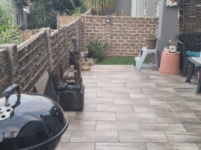 A paved outdoor patio area featuring brick boundary walls and a covered section, providing a functional space for outdoor relaxation.