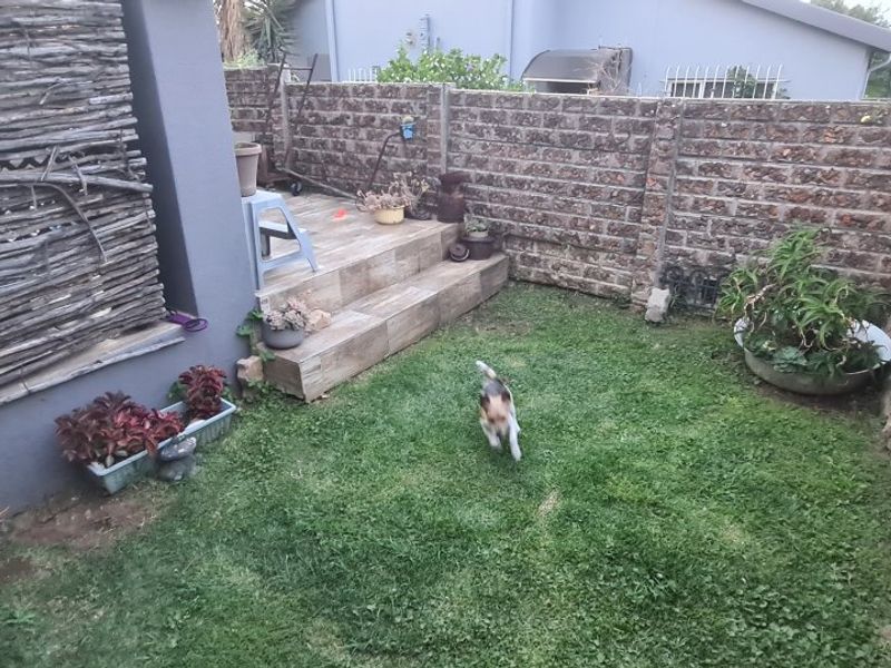 A private rear garden area featuring a small lawn, tiled patio steps, and secure brick boundary walls.