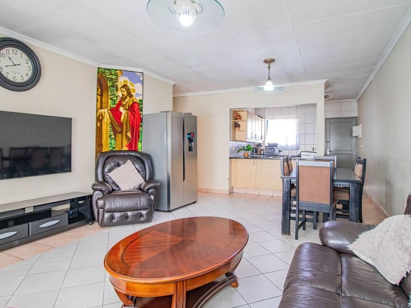 Open-plan living and dining area featuring tiled floors and a functional kitchen with built-in cabinetry, creating a cohesive and practical living space.