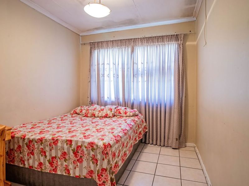A bedroom featuring tiled flooring and a ceiling-mounted light fixture, showing signs of wear on the ceiling surface.