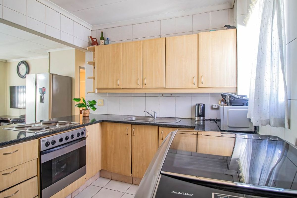 A functional kitchen featuring light wood cabinetry, granite countertops, a built-in oven with hob, and tiled finishes throughout.