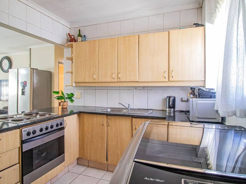A functional kitchen featuring light wood cabinetry, granite countertops, a built-in oven with hob, and tiled finishes throughout.