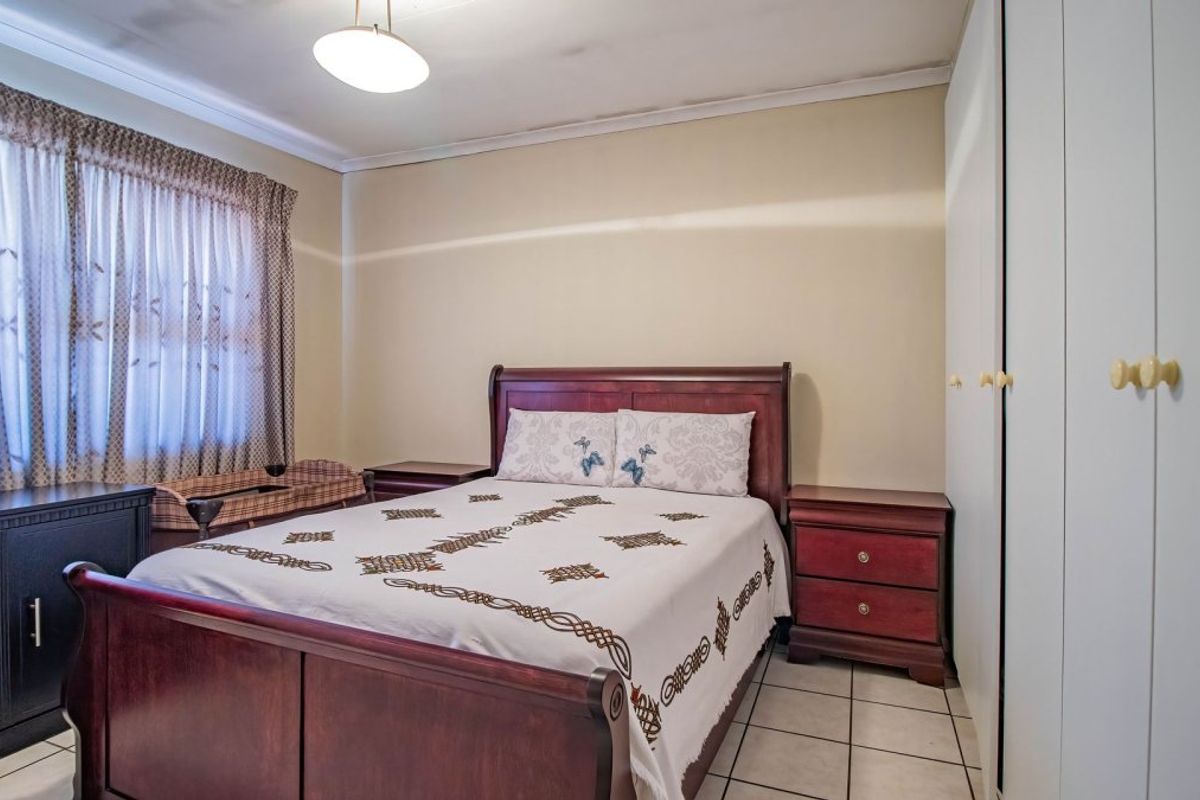 A bedroom featuring built-in cupboards, tiled flooring, and ceiling cornice, with visible signs of ceiling staining.