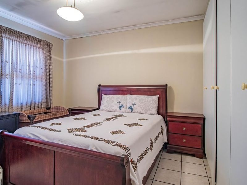 A bedroom featuring built-in cupboards, tiled flooring, and ceiling cornice, with visible signs of ceiling staining.