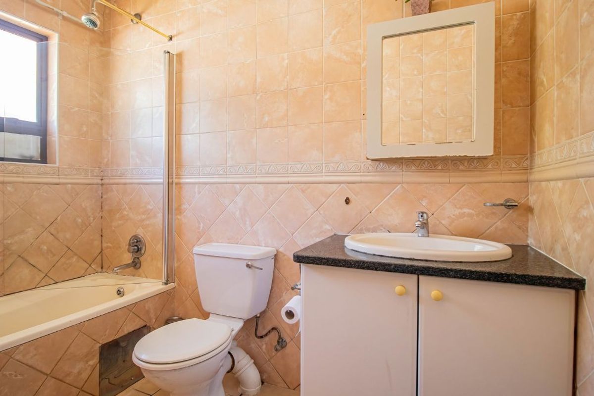 A dated bathroom featuring a bathtub with shower, vanity cabinet with granite countertop, and full-height ceramic wall tiling.