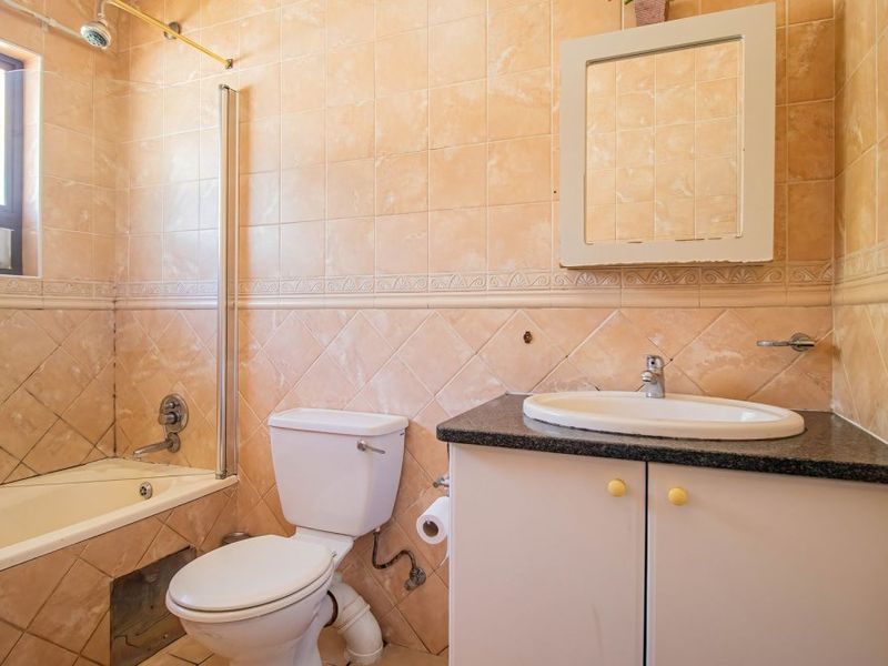 A dated bathroom featuring a bathtub with shower, vanity cabinet with granite countertop, and full-height ceramic wall tiling.