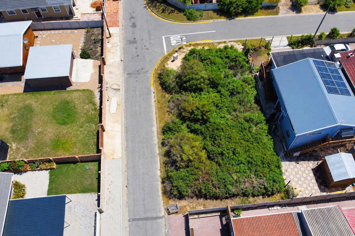 An aerial view of a vacant residential plot situated on a corner lot, surrounded by established residential properties and paved street infrastructure.