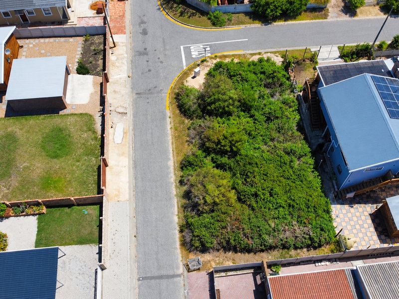 An aerial view of a vacant residential plot situated on a corner lot, surrounded by established residential properties and paved street infrastructure.