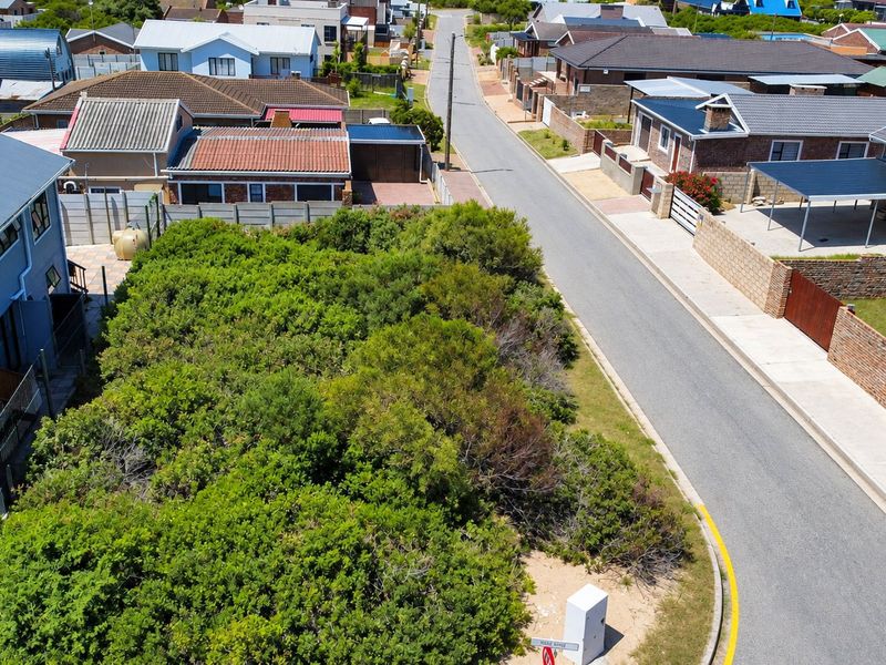 Aerial view of a vacant residential plot covered in dense vegetation, situated in a developed suburban street.