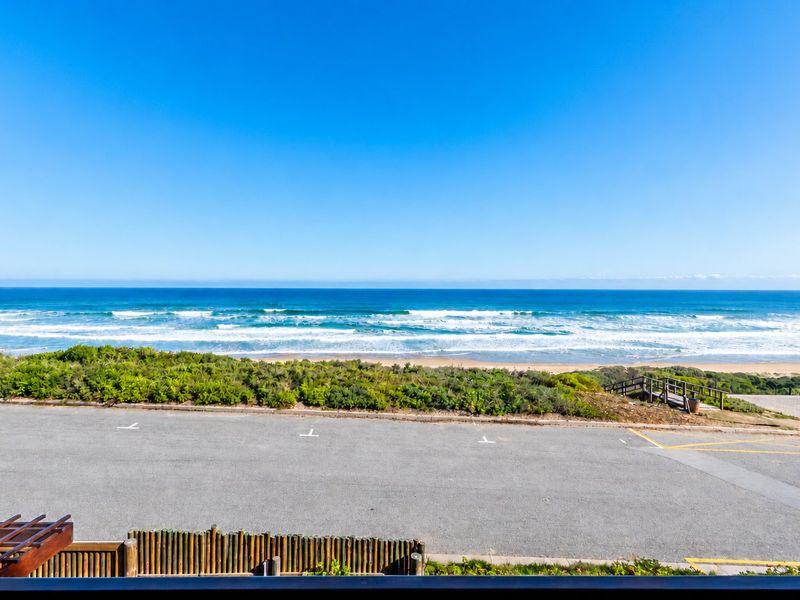 A scenic elevated view overlooking the ocean, sandy beach, and coastal vegetation with a pedestrian access path.