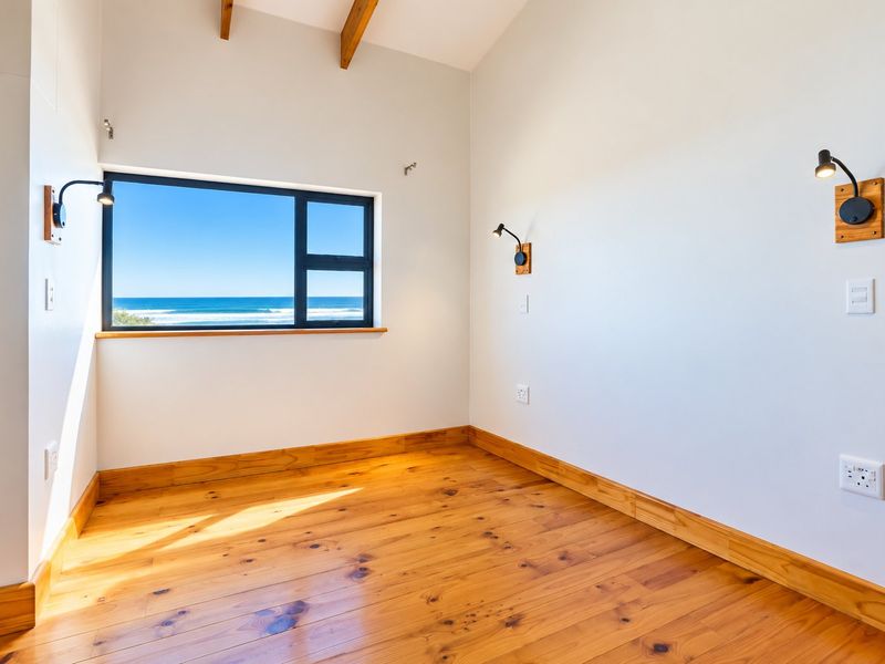A bright, empty bedroom featuring polished timber flooring, exposed ceiling beams, and a large window offering a clear ocean view.