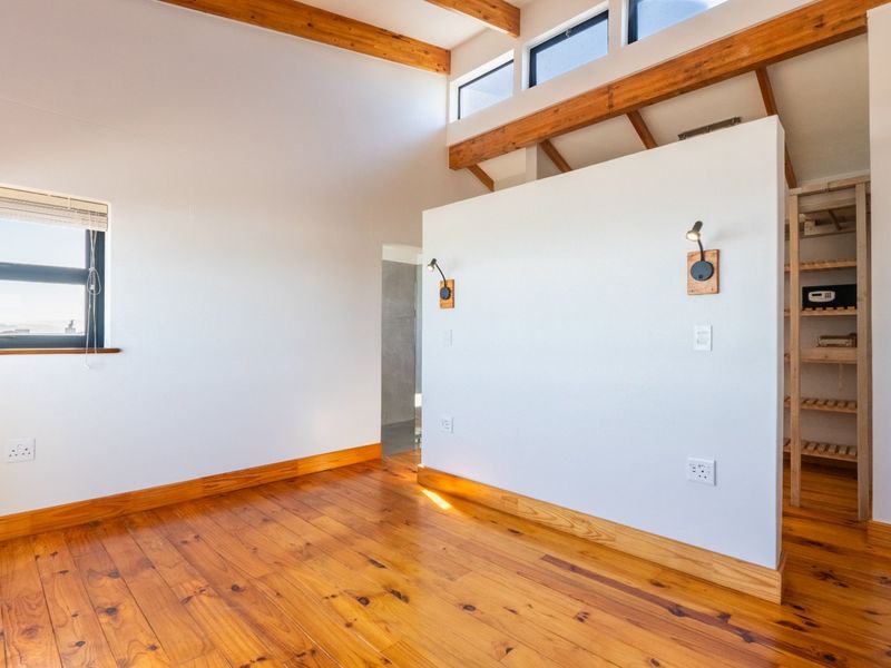 Bright bedroom featuring exposed timber ceiling beams, polished timber flooring, clerestory windows for natural light, and a convenient built-in storage area.