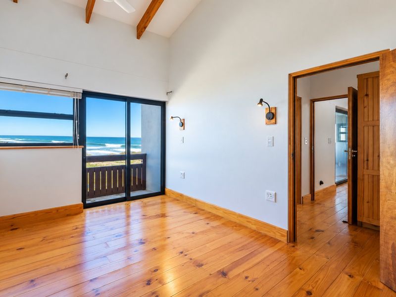 Bright bedroom featuring polished timber flooring, exposed ceiling beams, and a sliding glass door opening to a balcony with ocean views.