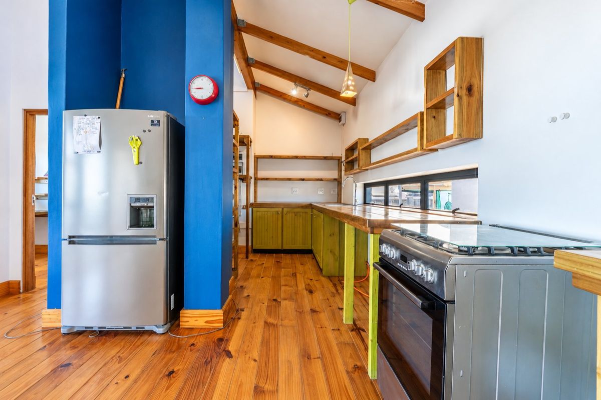 A rustic-style kitchen featuring exposed timber ceiling beams, wooden countertops, open shelving, and a freestanding gas stove with warm timber flooring.