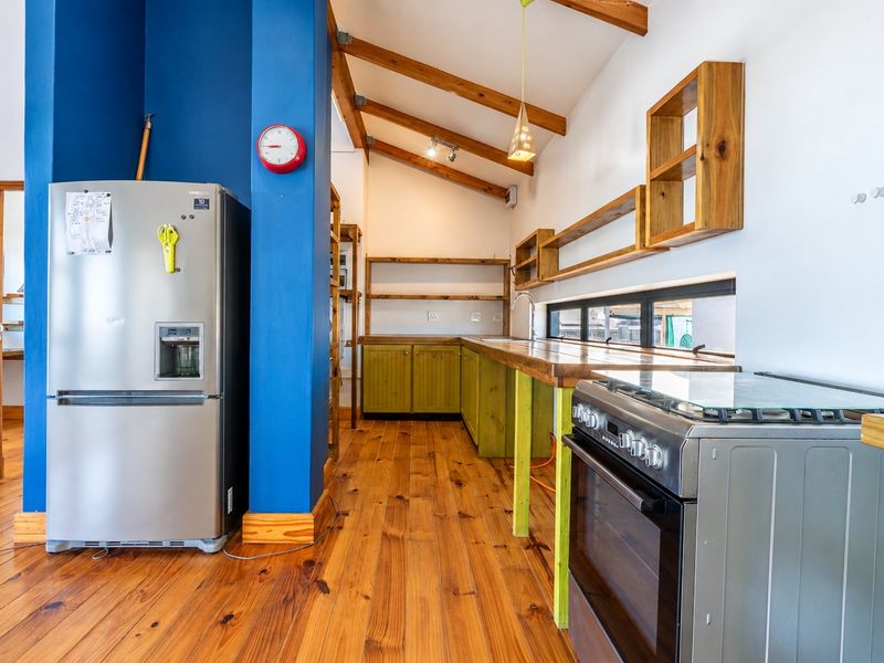 A rustic-style kitchen featuring exposed timber ceiling beams, wooden countertops, open shelving, and a freestanding gas stove with warm timber flooring.