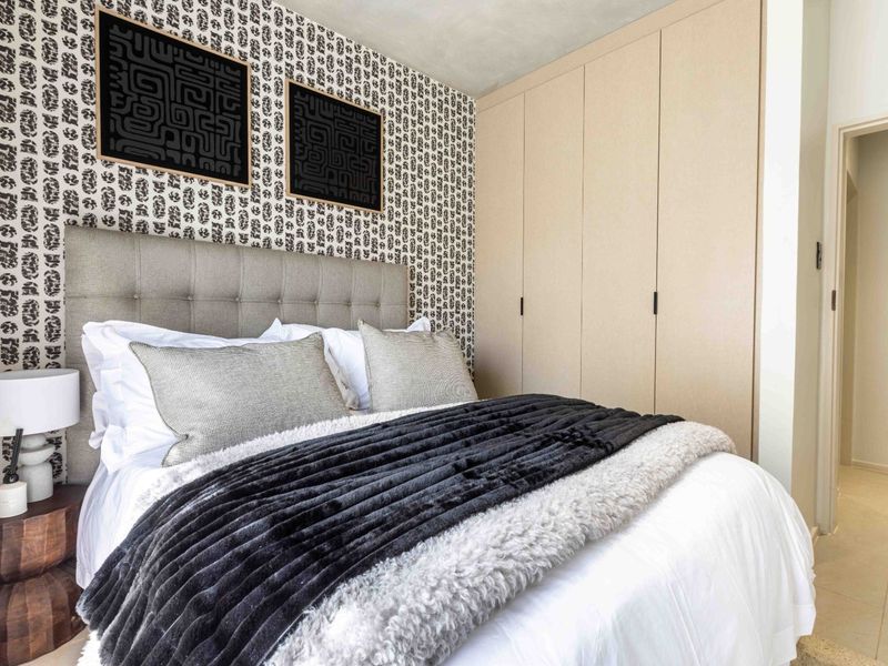 A well-maintained bedroom featuring floor-to-ceiling built-in cupboards, patterned feature wallpaper, and neutral tiled flooring.