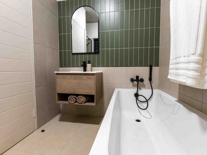 Modern bathroom featuring a wall-mounted vanity, integrated sink, and a sleek bathtub with matte black fixtures and stylish green tiled accents.