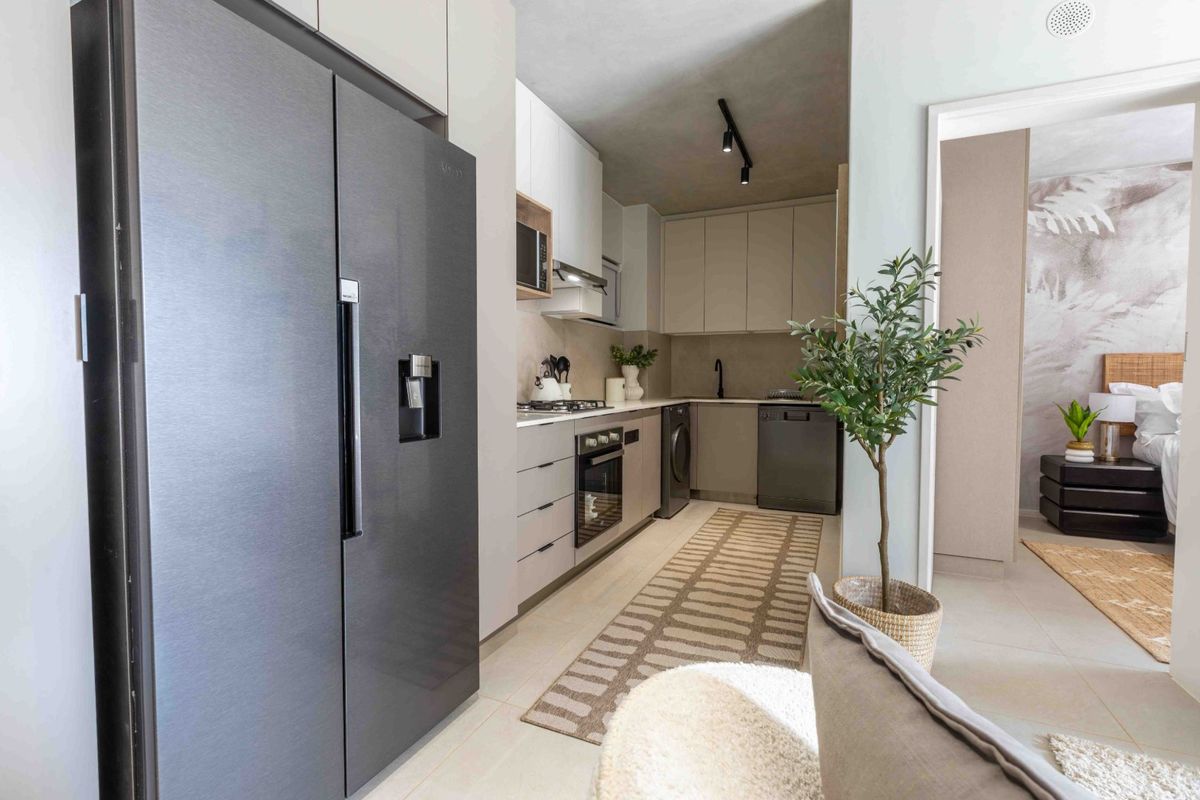 Modern galley-style kitchen featuring sleek cabinetry, integrated appliances, gas cooktop, and contemporary track lighting, seamlessly flowing into the adjacent living and bedroom areas.