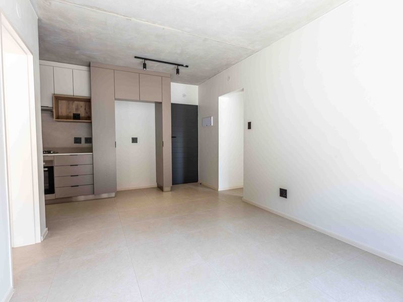 Modern open-plan living area featuring a sleek kitchen with built-in cabinetry, integrated oven, hob, tiled flooring, and a contemporary exposed concrete ceiling.