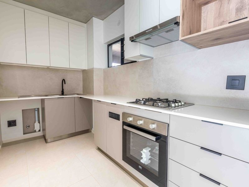 Modern kitchen featuring sleek white and grey cabinetry, stone countertops, a gas hob, built-in oven, and high-quality finishes throughout.