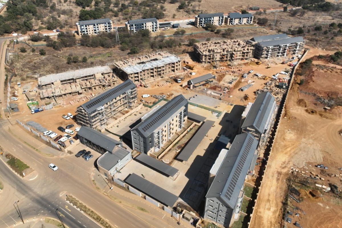 Aerial view of a residential apartment development complex under construction, featuring multiple multi-story buildings, solar panels, and paved parking areas.