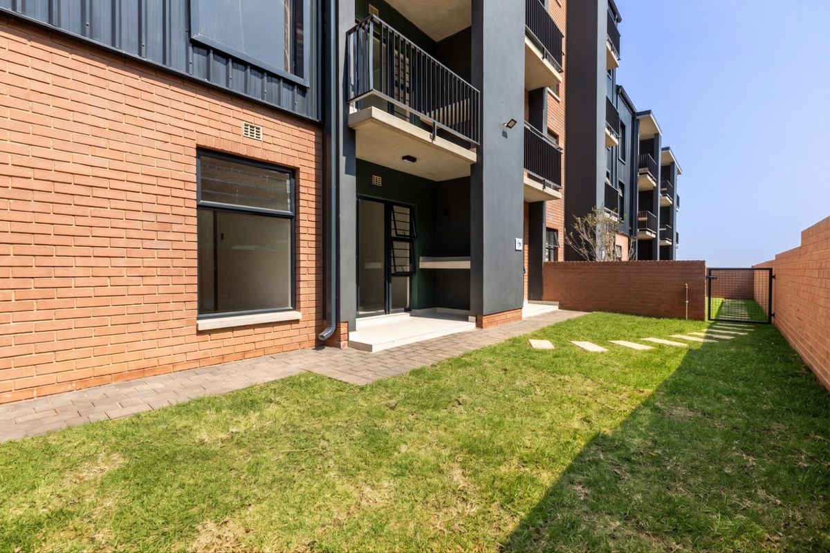 A well-maintained rear exterior view of the apartment building featuring a private garden, paved patio area, and balcony access.
