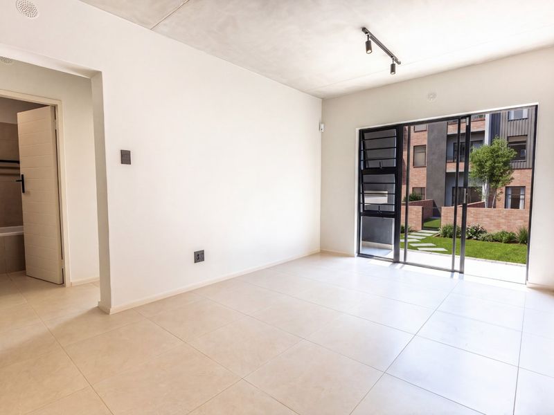 Bright, modern open-plan living area featuring neutral tiled flooring, exposed concrete ceiling, and large sliding glass doors opening to a private garden view.