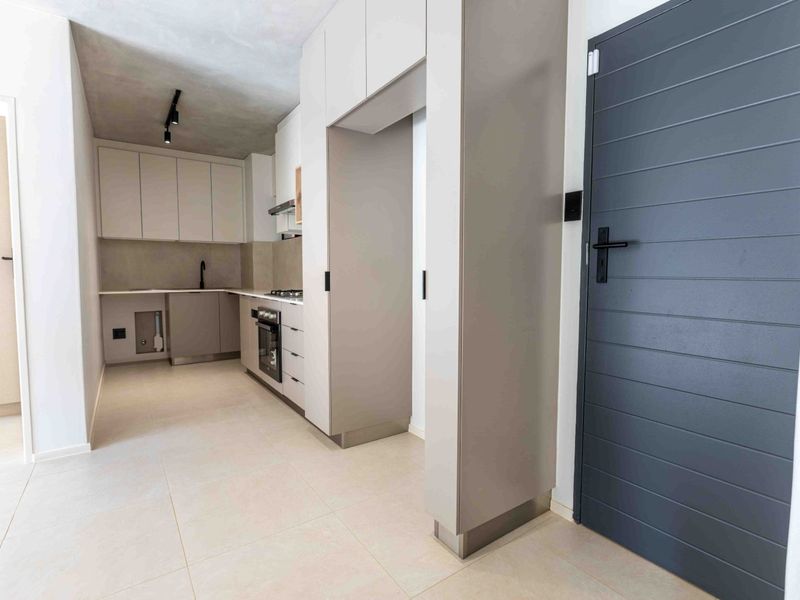 Modern kitchen featuring sleek built-in cabinetry, integrated oven, gas hob, and high-quality tiled flooring in a clean, contemporary apartment setting.