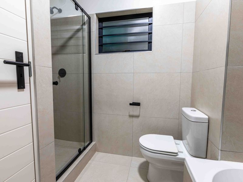 A modern, well-maintained bathroom featuring a glass-enclosed shower, neutral wall and floor tiling, and a clean, contemporary toilet fixture.