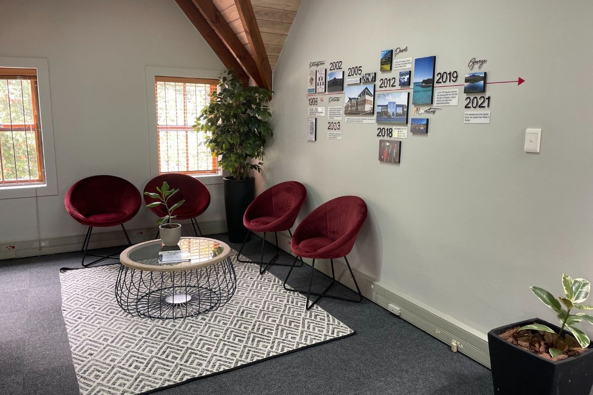A professional office waiting area featuring exposed timber rafters, carpeted flooring, and natural light from casement windows.