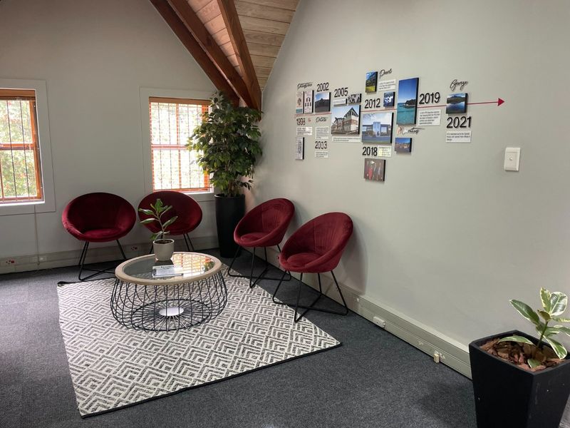 A professional office waiting area featuring exposed timber rafters, carpeted flooring, and natural light from casement windows.