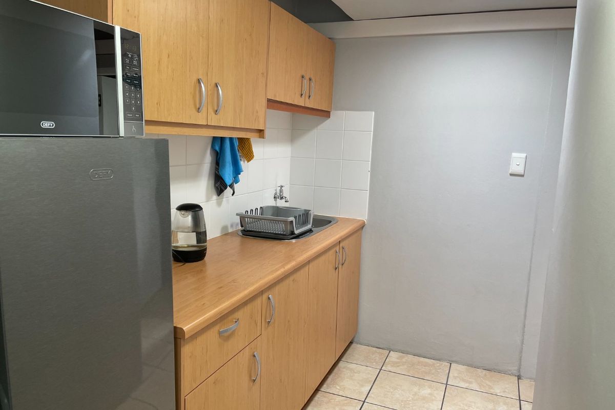 A compact kitchen area featuring light wood-finish cabinetry, laminate countertops, a stainless steel sink, and neutral ceramic floor tiling.